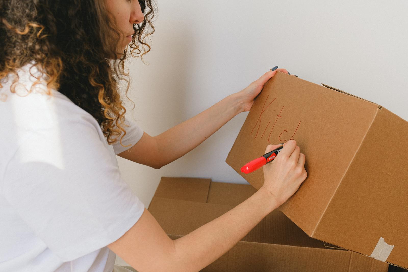 Woman organizing and labeling cardboard boxes for moving indoors.